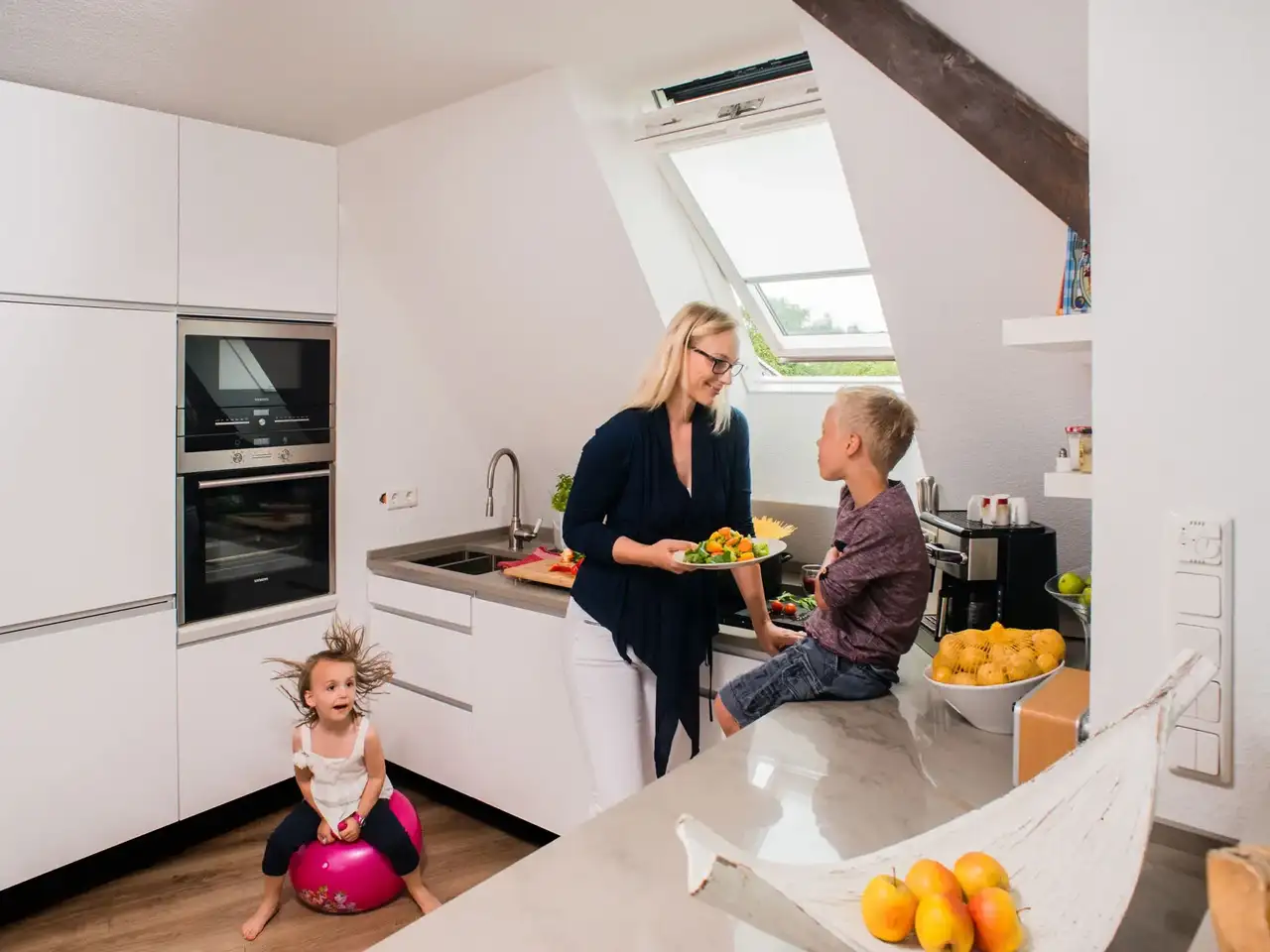 Frau steht mit zwei Kindern in einer hellen Küche und bereitet das Essen vor | VELUX Magazin