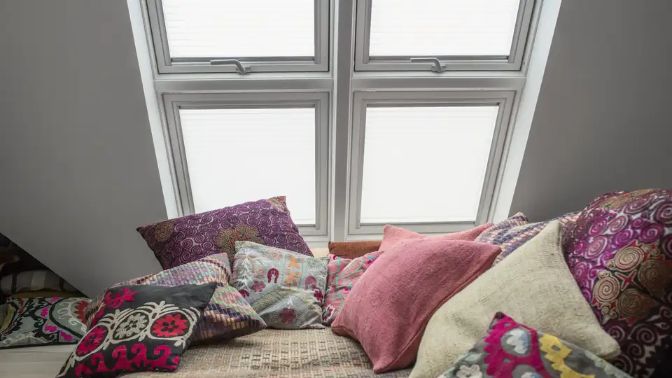 Coussins décoratifs aux motifs rétro sous des fenêtres de toit VELUX avec stores intérieurs.