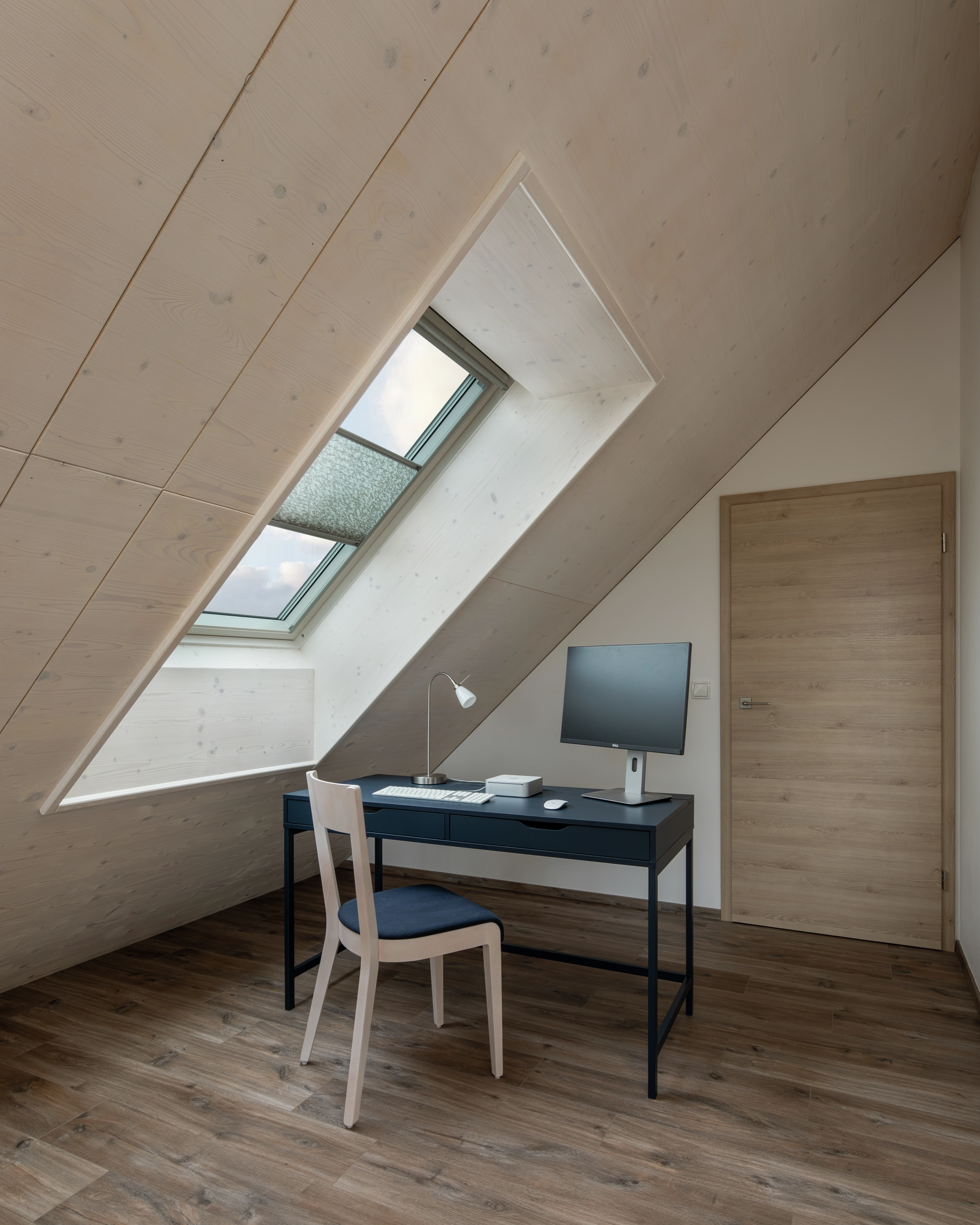 Attic home office with sloped ceiling and VELUX roof window, natural light entering.