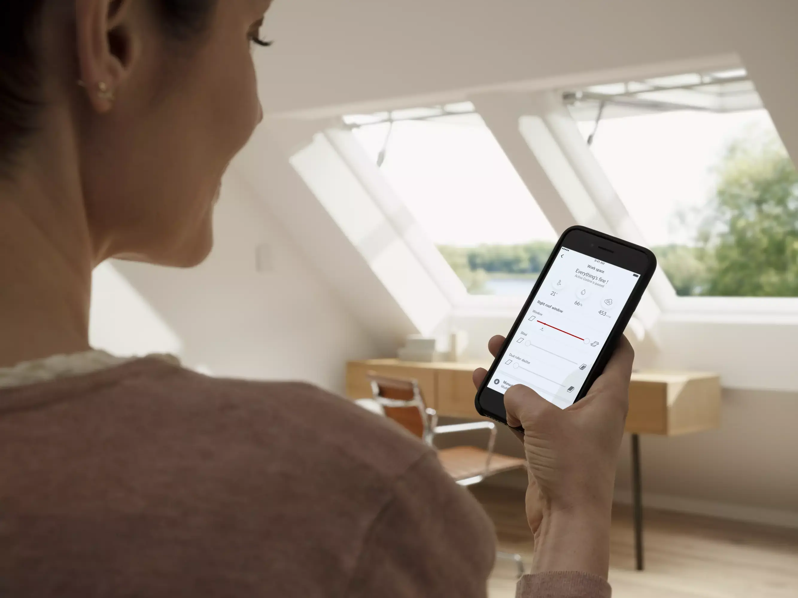 Smartphone avec application de maison intelligente dans une chambre de comble bien éclairée avec fenêtre de toit VELUX.