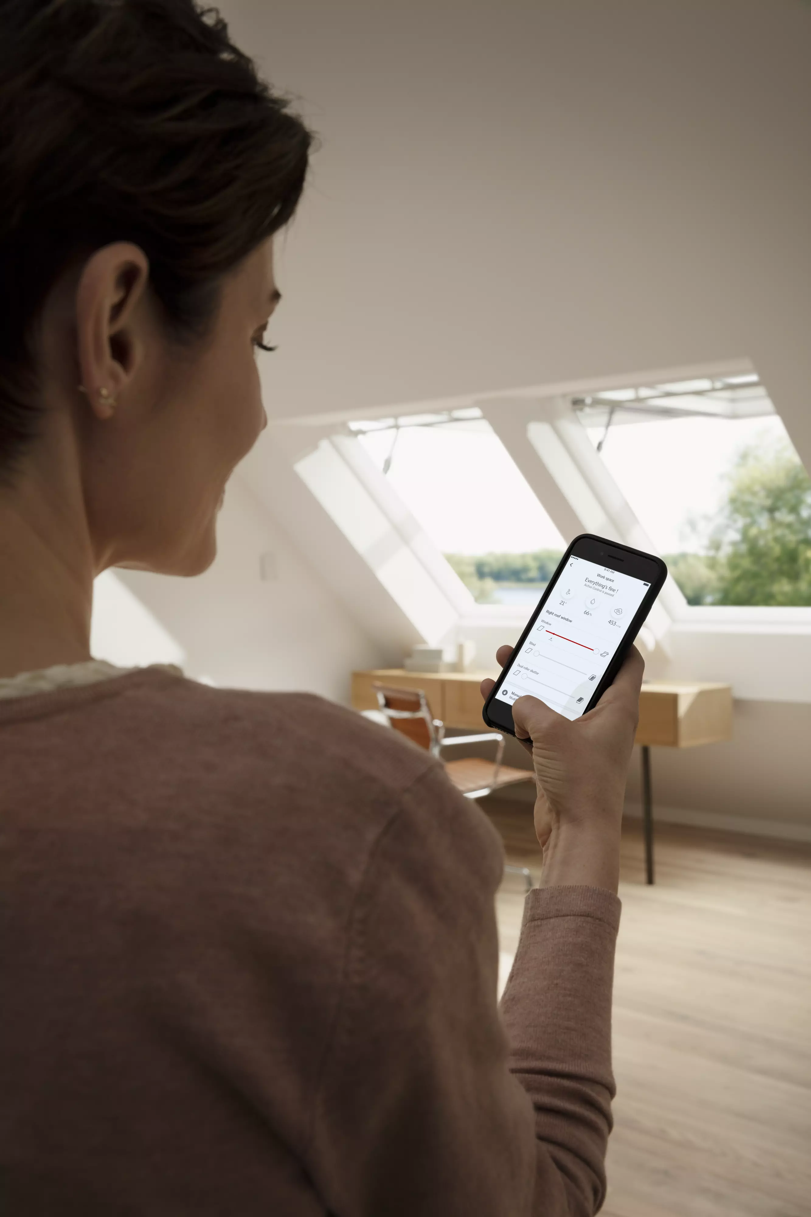 Personne utilisant une application de maison intelligente dans un bureau à domicile ensoleillé avec une fenêtre de toit VELUX.