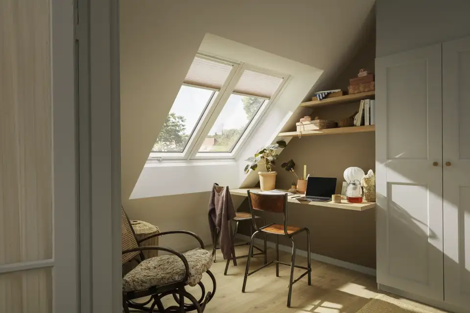 Bureau sous les combles avec deux fenêtres de toit VELUX équipées de stores plissés tamisants à demi-baissés 