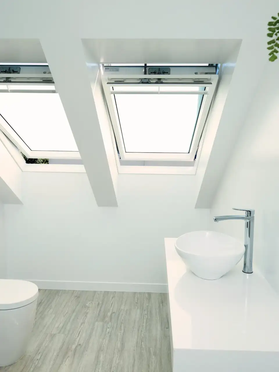 Small attic bathroom with two VELUX roof windows bringing daylight onto white walls and basin.