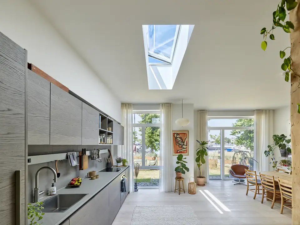 Moderna otvorena kuhinja i trpezarija s VELUX krovnim prozorom koji ispunjava prostor prirodnim svjetlom i dodatno naglašava svijetlu, prozračnu atmosferu | VELUX.
