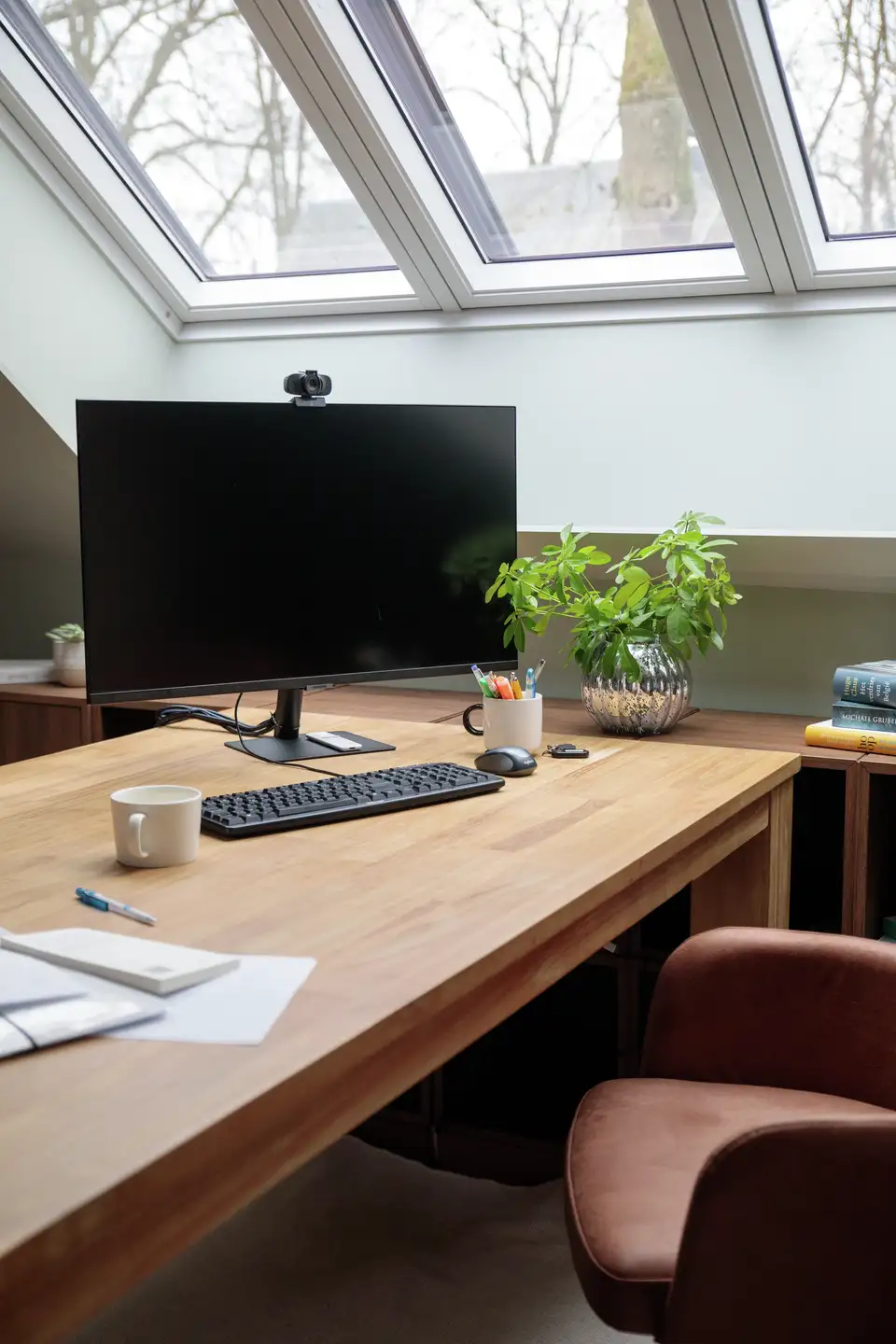 Home office in mansarda con finestre per tetti e una scrivania in legno.