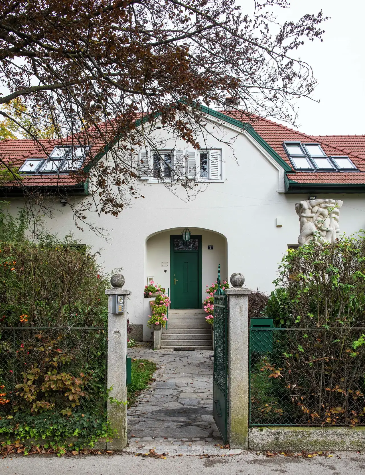 Front view of a charming house with a green door and roof windows, framed by trees and shrubs. | VELUX