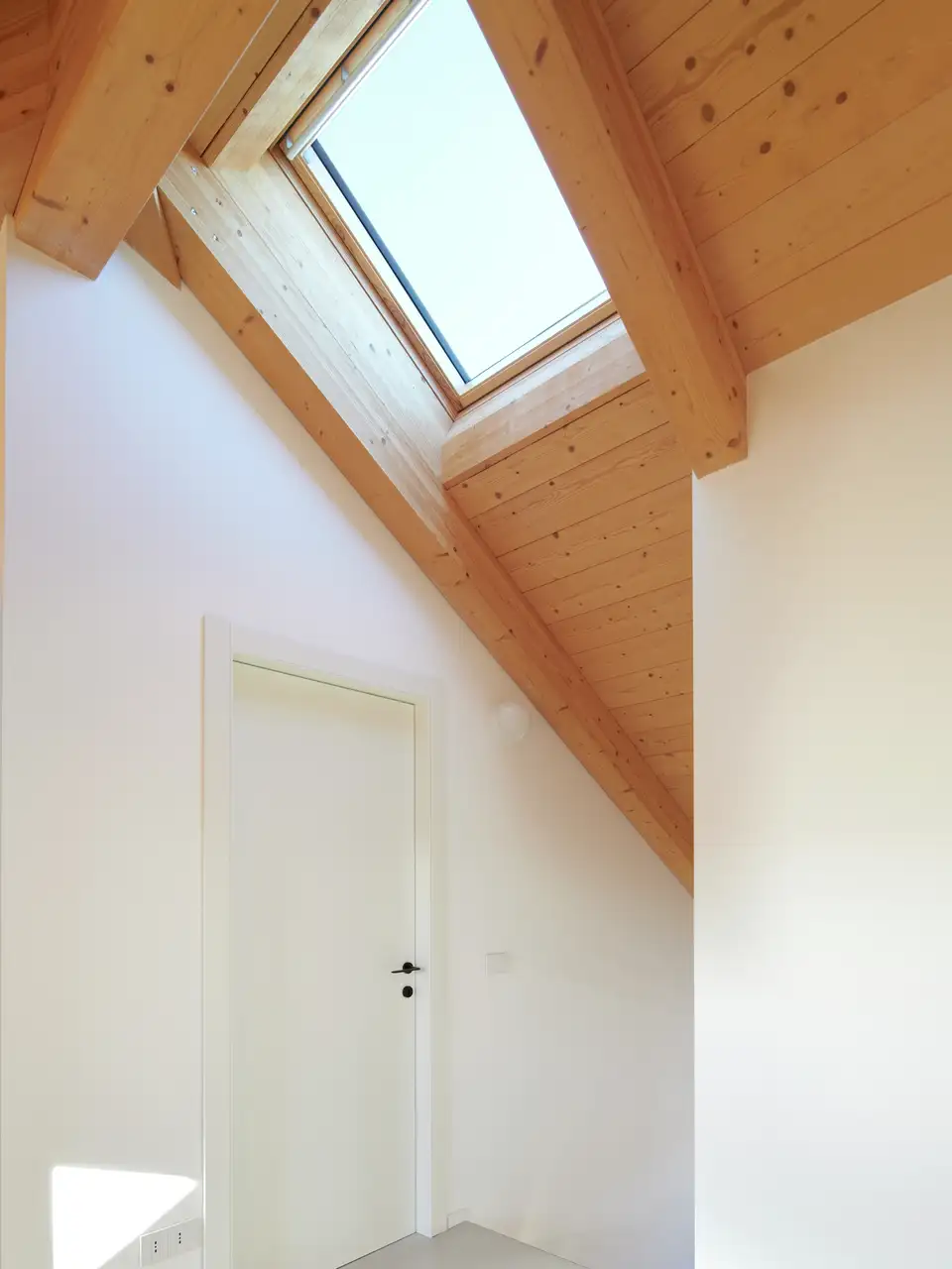 Vivienda con tejados abuhardillados con techo de madera y ventana de tejado. 
