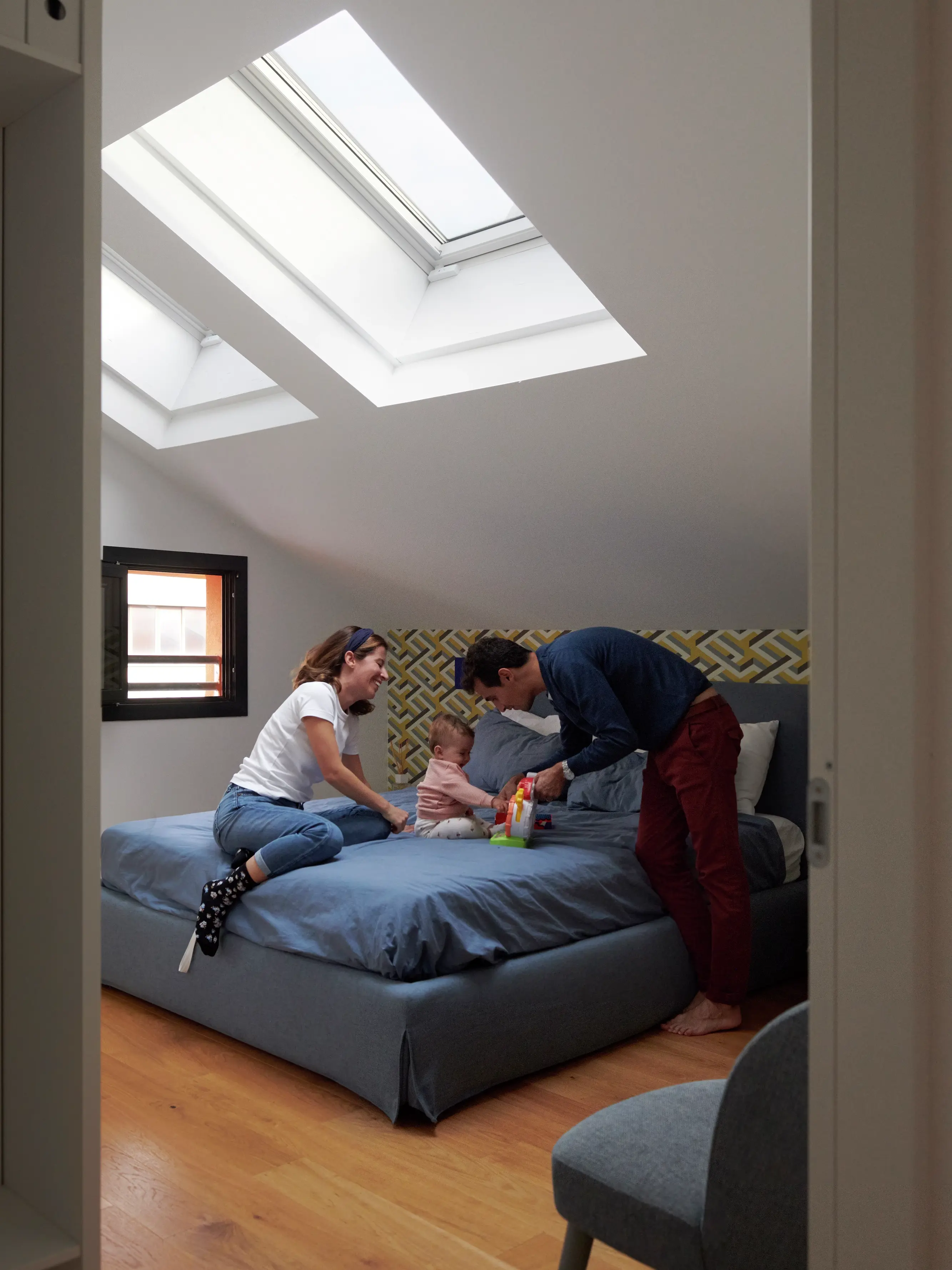 Famiglia che gioca sul letto in una stanza illuminata dal sole con una finestra per tetti VELUX.