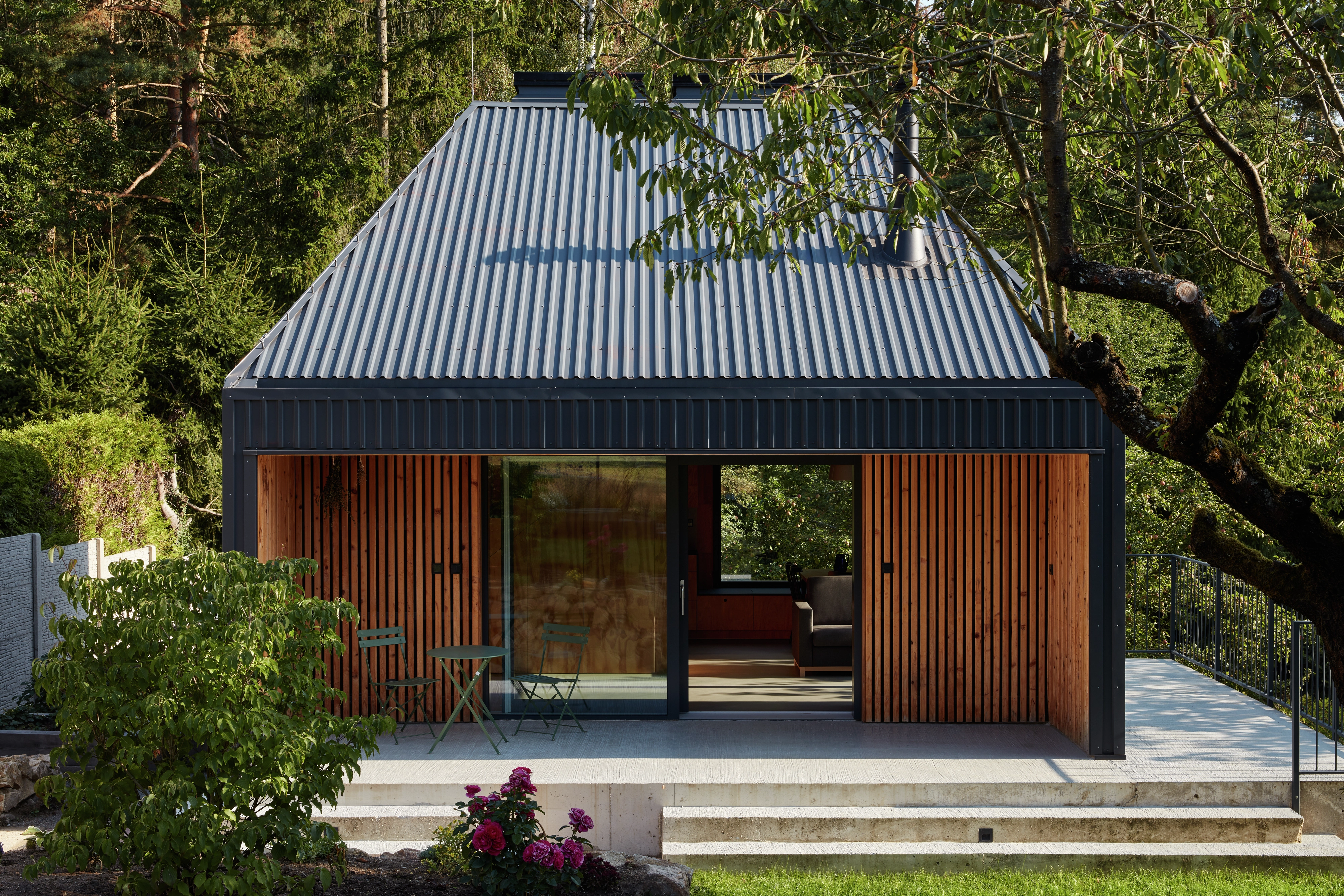 Modern house with metal roof and wooden facade, surrounded by greenery.