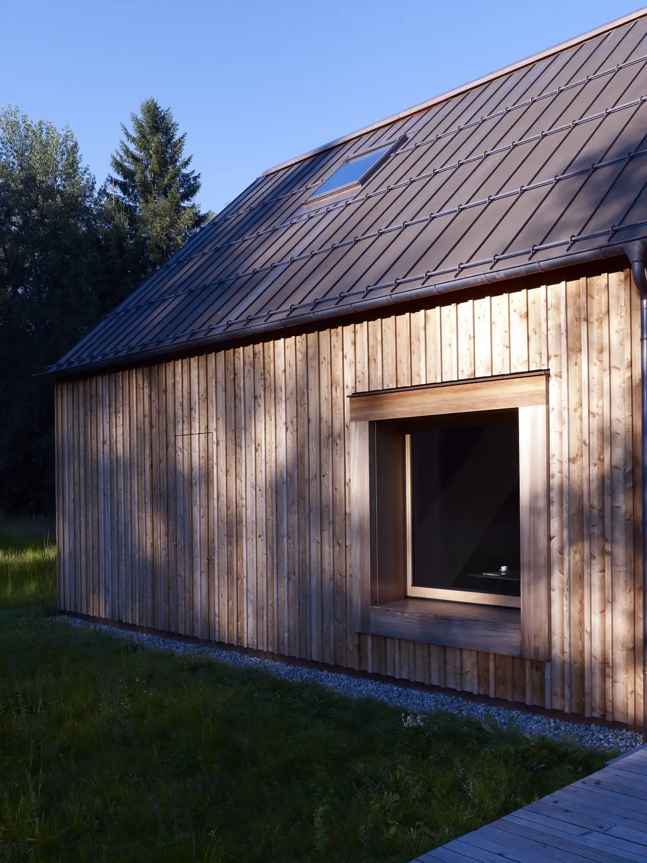 Lesena hiša s kovinsko streho in strešnim oknom VELUX obdana z zelenjem.