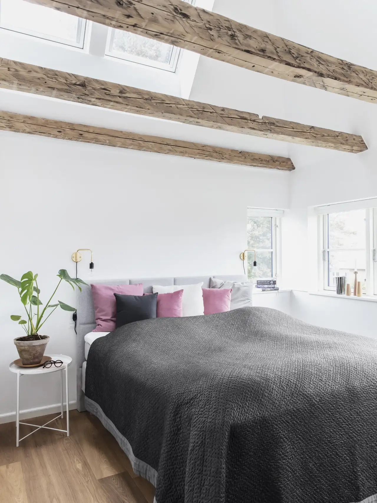 Camera da letto luminosa con travi a vista, letto con testata imbottita grigia e cuscini colorati