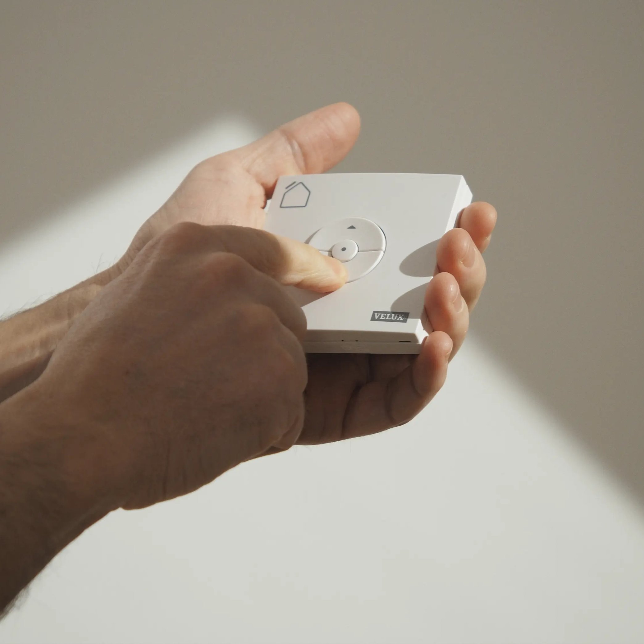 Hands holding a VELUX remote control, pressing the central button.