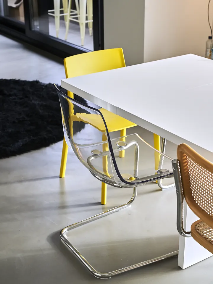 1950'lerden esinlenerek tasarlanmış, beyaz bir masa, hasır sandalyeler ve şık, şeffaf bir plastik sandalye.