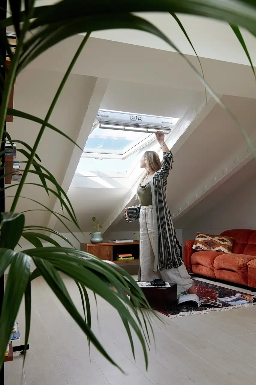 Pièce au grenier avec plafond en pente et fenêtre de toit VELUX, personne ouvrant la fenêtre.