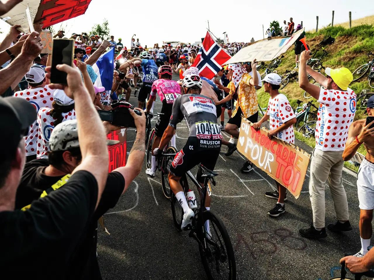 Kolesarji drvijo skozi navijaško množico med Tour de France s številkami VELUX na hrbtih.