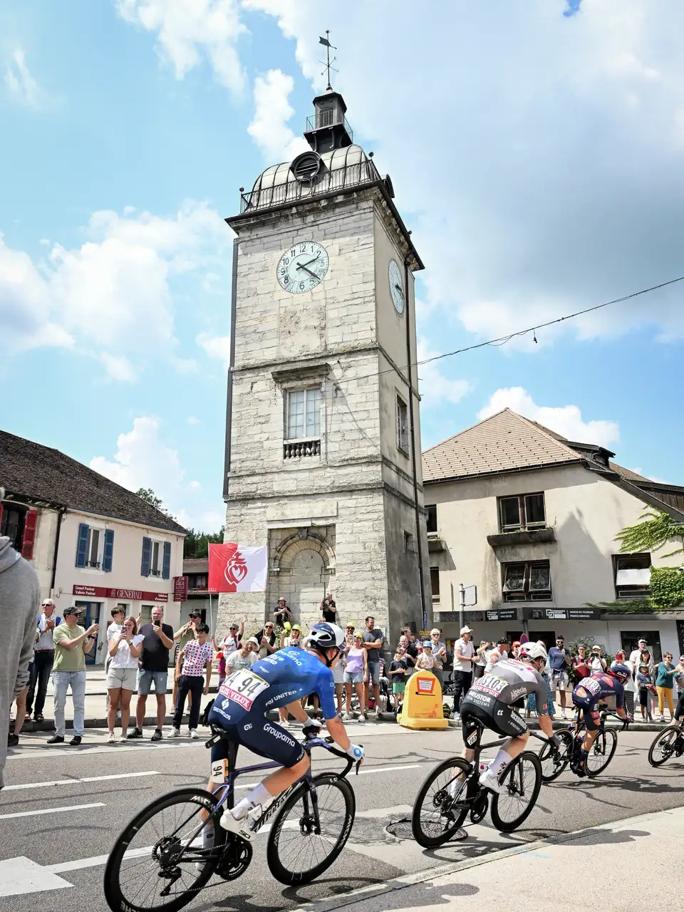 Kolesarska prireditev z navijači Tour de France in logotipom VELUX v mestnem okolju.