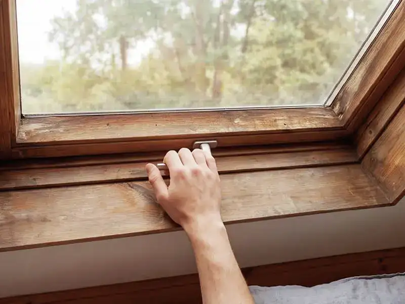 main ouvrant une fenêtre de toit VELUX avec cadre en bois