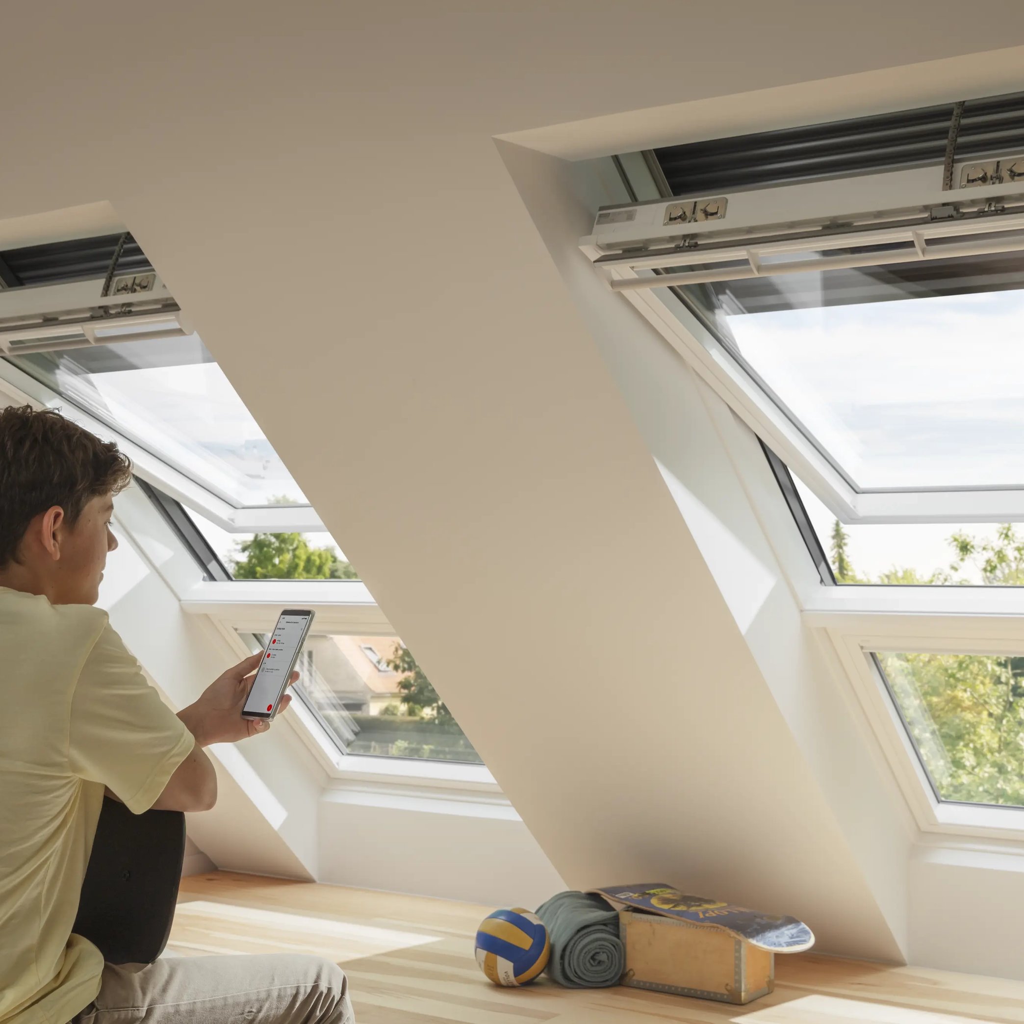 Attic room with VELUX roof windows, young person using smartphone.