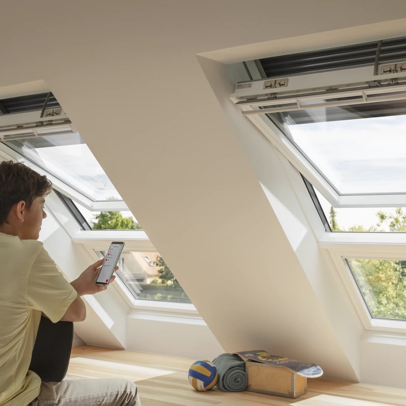 Attic room with VELUX roof windows, young person using smartphone.