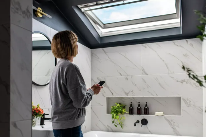 Frau öffnet elektrisches Dachfenster über Badewanne im modernen Bad | VELUX Magazin