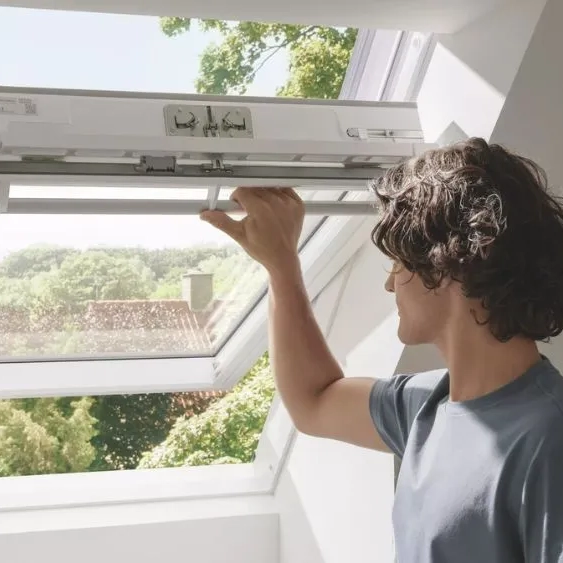 Person opening a VELUX roof window in a bright attic room.