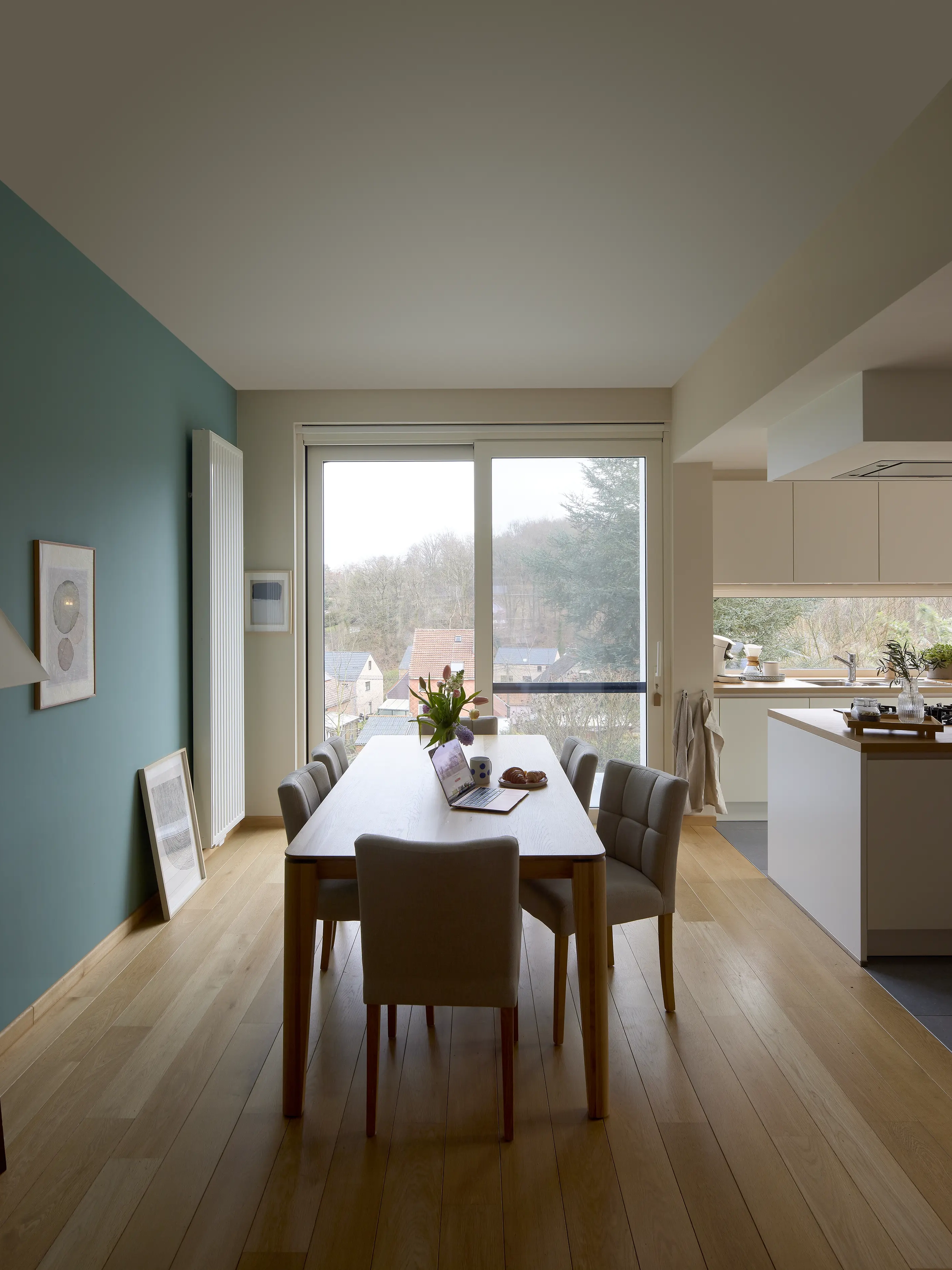 Zona pranzo con tavolo in legno, sedie e ampie finestre verticali, cucina in stile moderno.