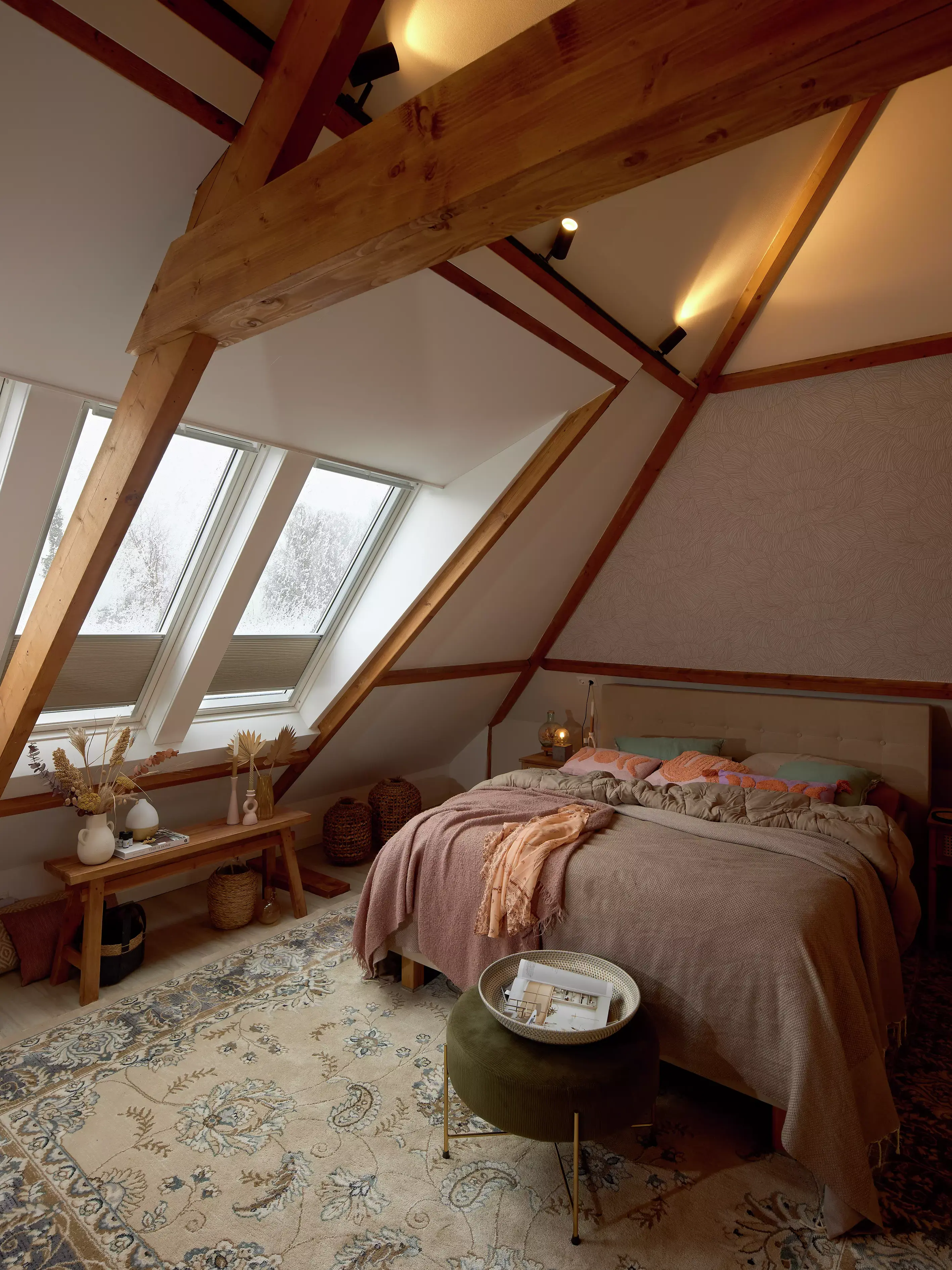 Chambre de comble avec poutres apparentes et fenêtres de toit VELUX, décorée dans des tons chaleureux.