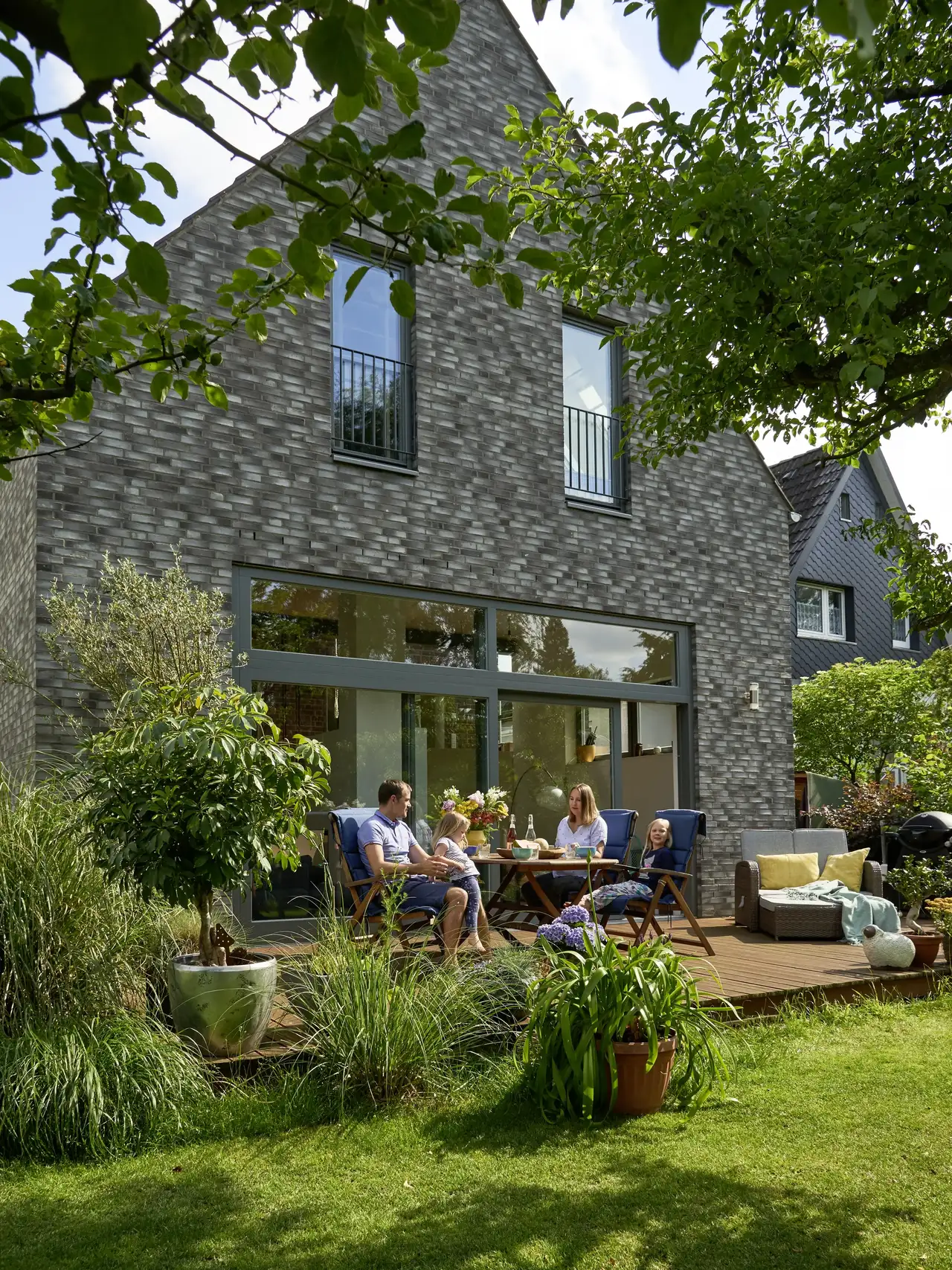 Familie mit zwei kleinen Töchtern frühstückt auf der Terrasse ihres Satteldach-Hauses | VELUX Magazin