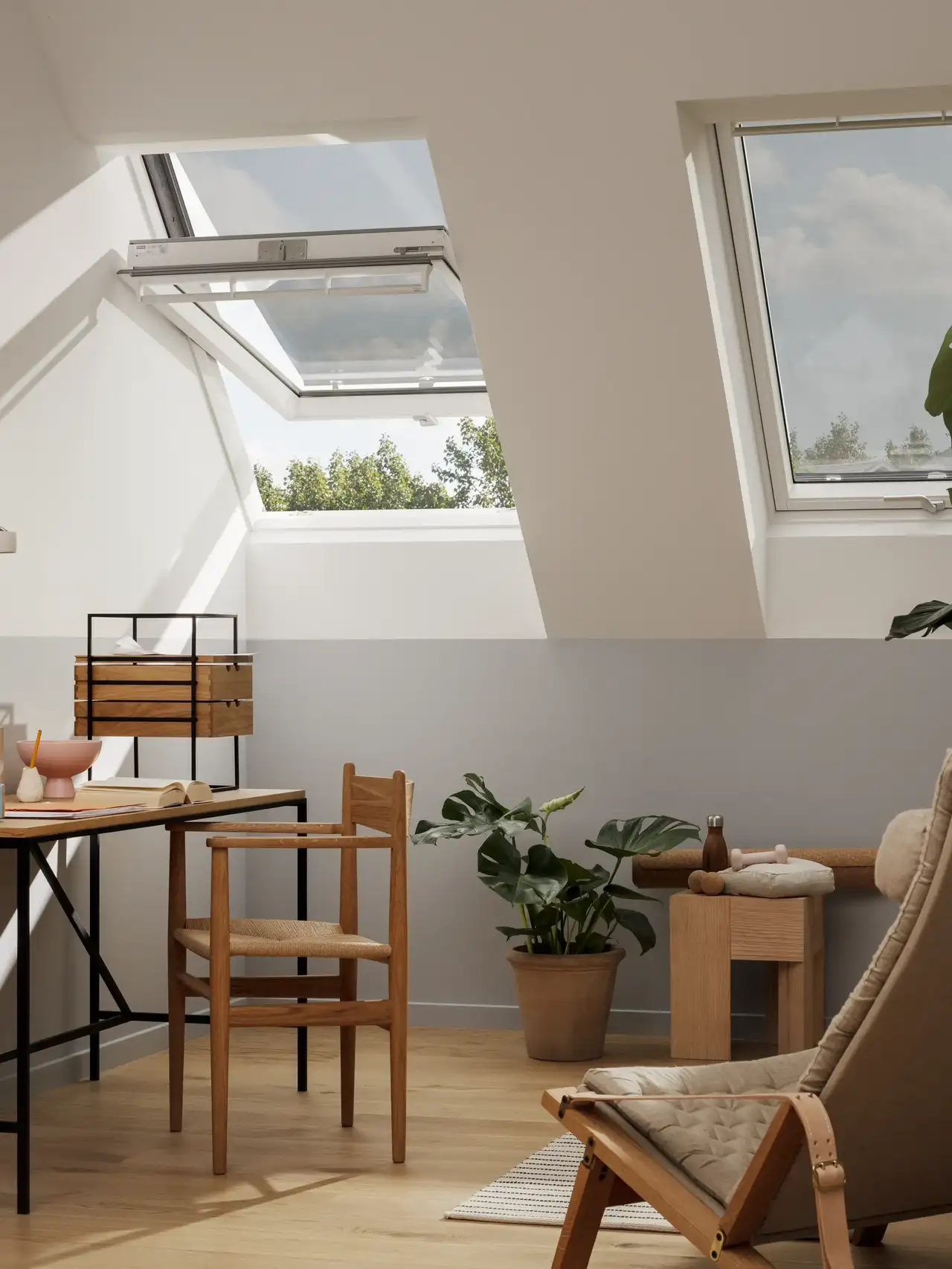 Home office in mansarda con grandi piante e finestre per tetti protette da tende parasole esterne.
