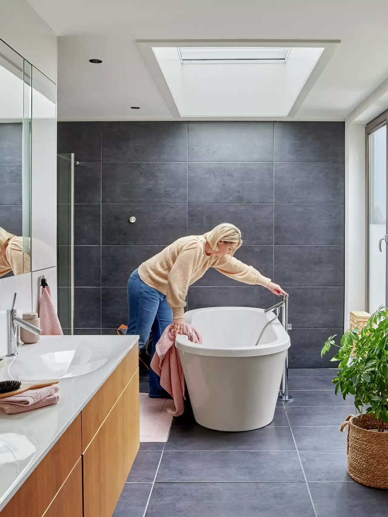Una donna fa entrare acqua in una vasca da bagno free standing posizionata sotto una finestra per tetti.