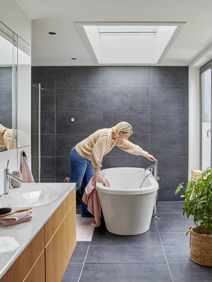 Frau putzt freistehende Badewanne unter einem Flachdachfenster | VELUX Magazin
