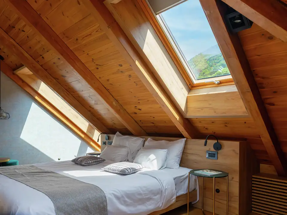Camera da letto in mansarda con soffitto spiovente in legno e finestre per tetti VELUX.
