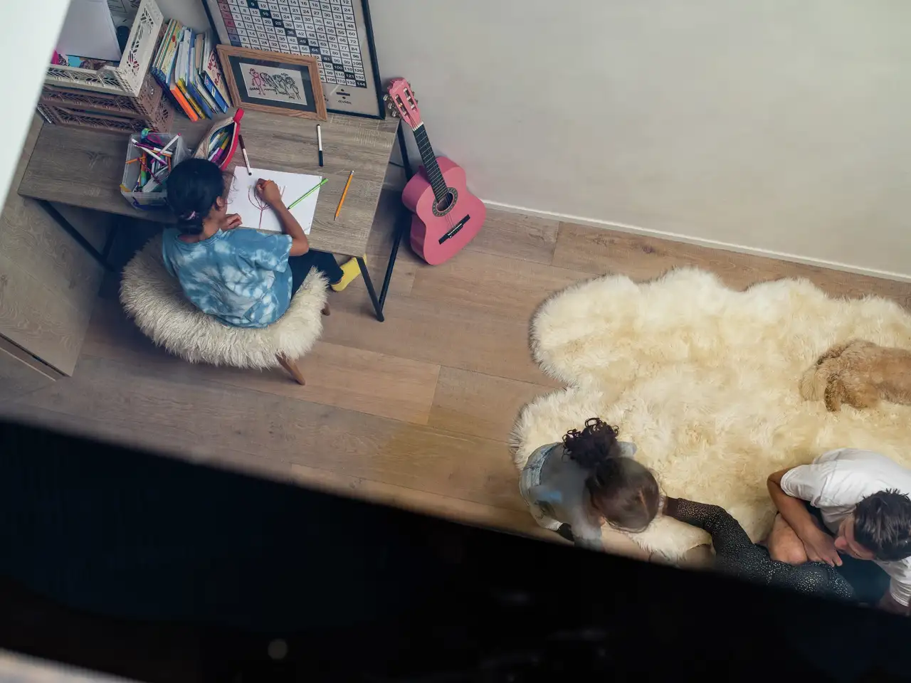 Blick durch das Flachdach-Fenster zeigt junges Mädchen beim Malen und ihre Geschwister beim Toben im hellen Kinderzimmer | VELUX Magazin