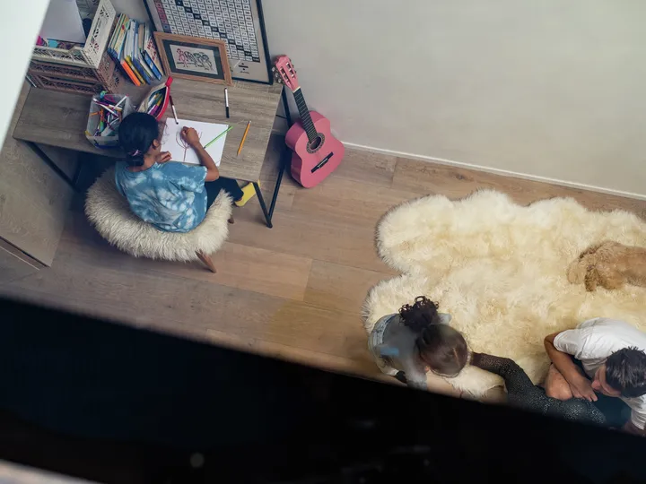 Blick durch das Flachdach-Fenster zeigt junges Mädchen beim Malen und ihre Geschwister beim Toben im hellen Kinderzimmer | VELUX Magazin