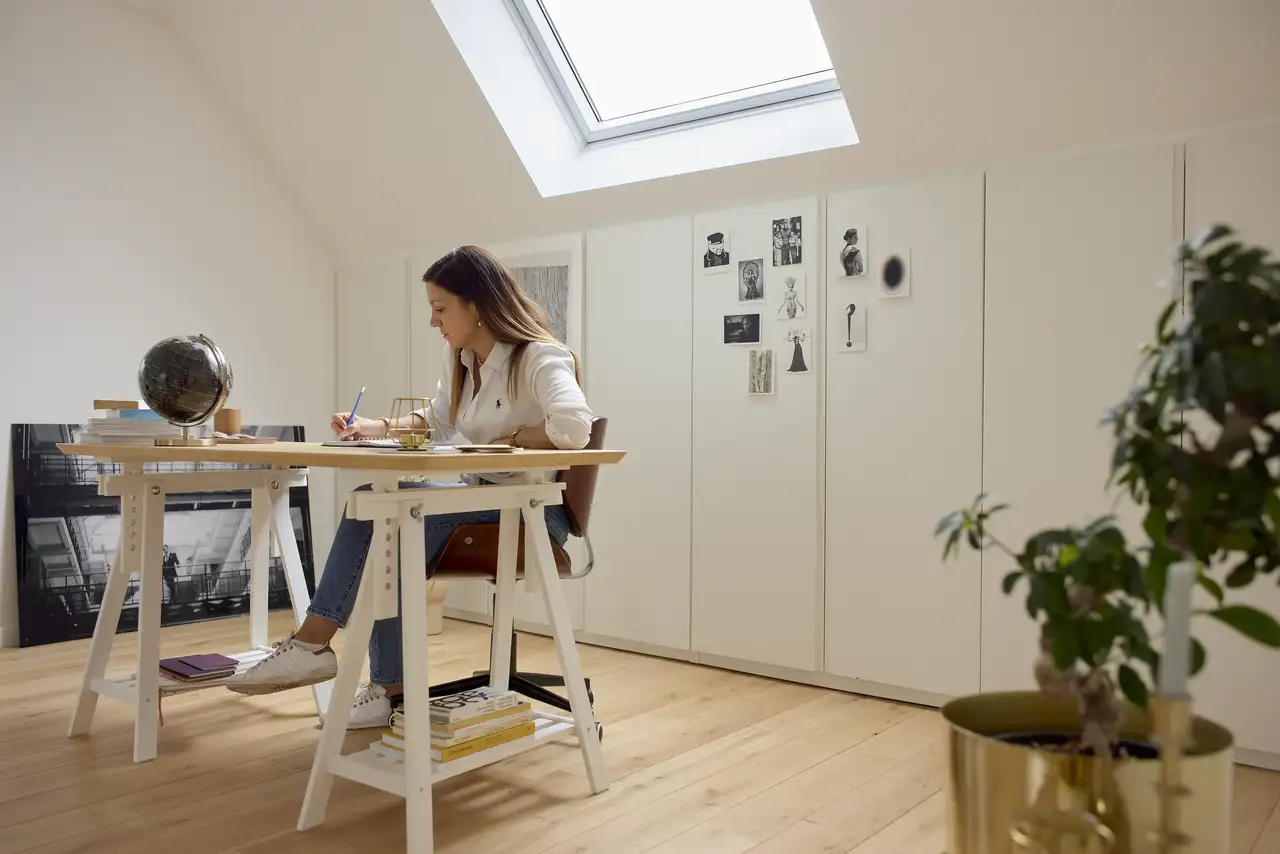 Espaço de trabalho no sótão com um teto inclinado e uma janela de telhado VELUX que deixa entrar luz natural. 