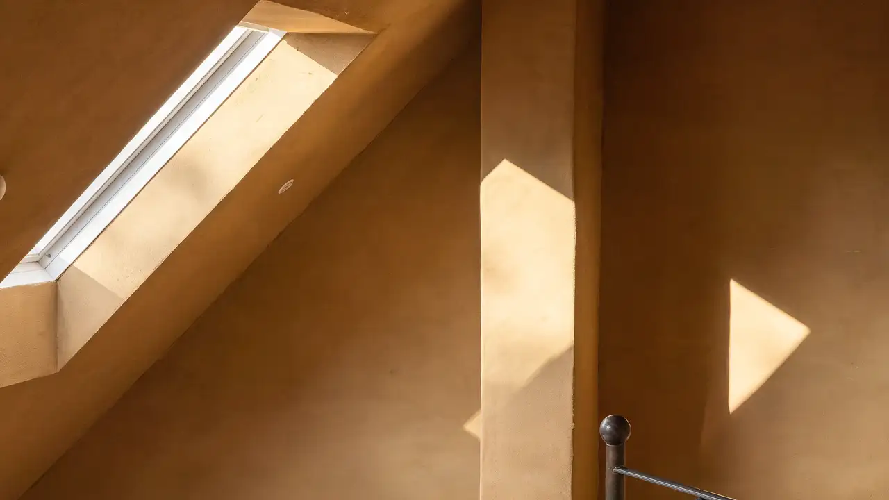 Sonnenlicht strömt durch ein VELUX Dachfenster und wirft sanfte Schatten auf eine warm getönte Wand. | VELUX Magazin
