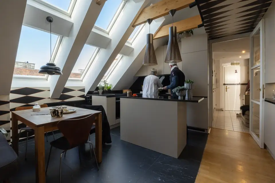 Cucina in mansarda con isola e tavolo quadrato posizionato sotto grandi finestre per tetti VELUX.