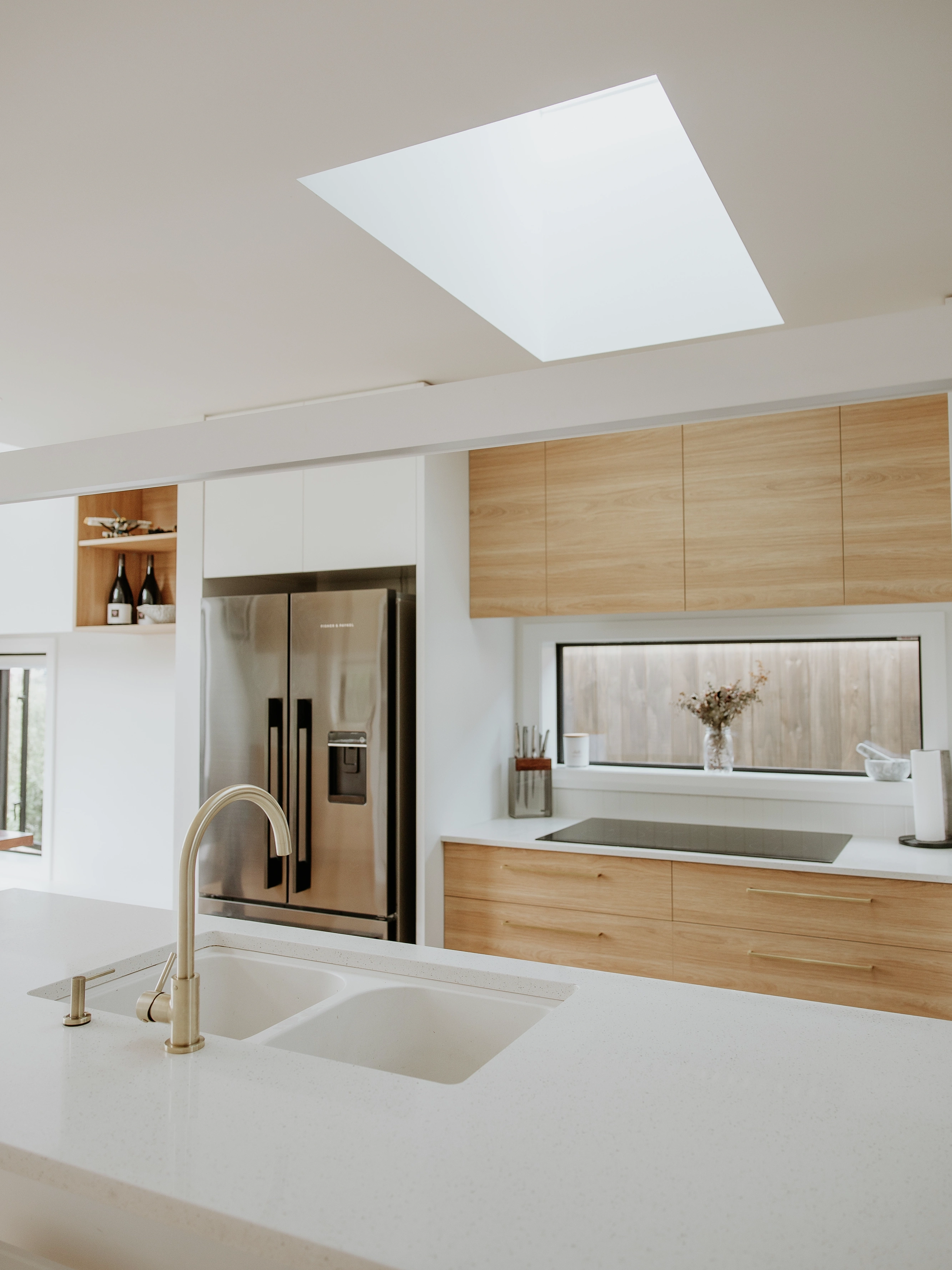 Modern kitchen with VELUX flat roof window bringing daylight over white island and wood cabinets.