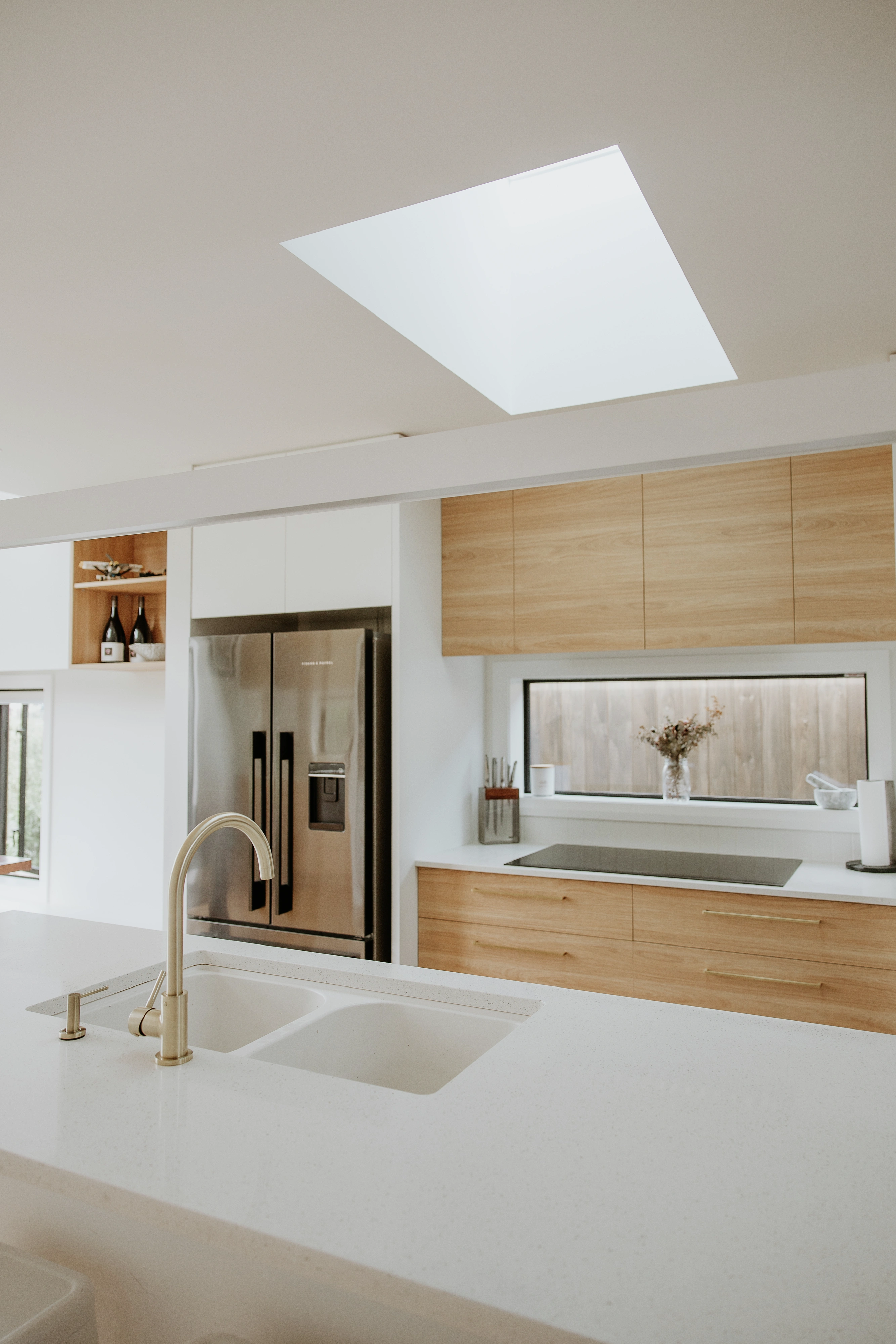 Modern kitchen with VELUX flat roof window bringing daylight over white island and wood cabinets.