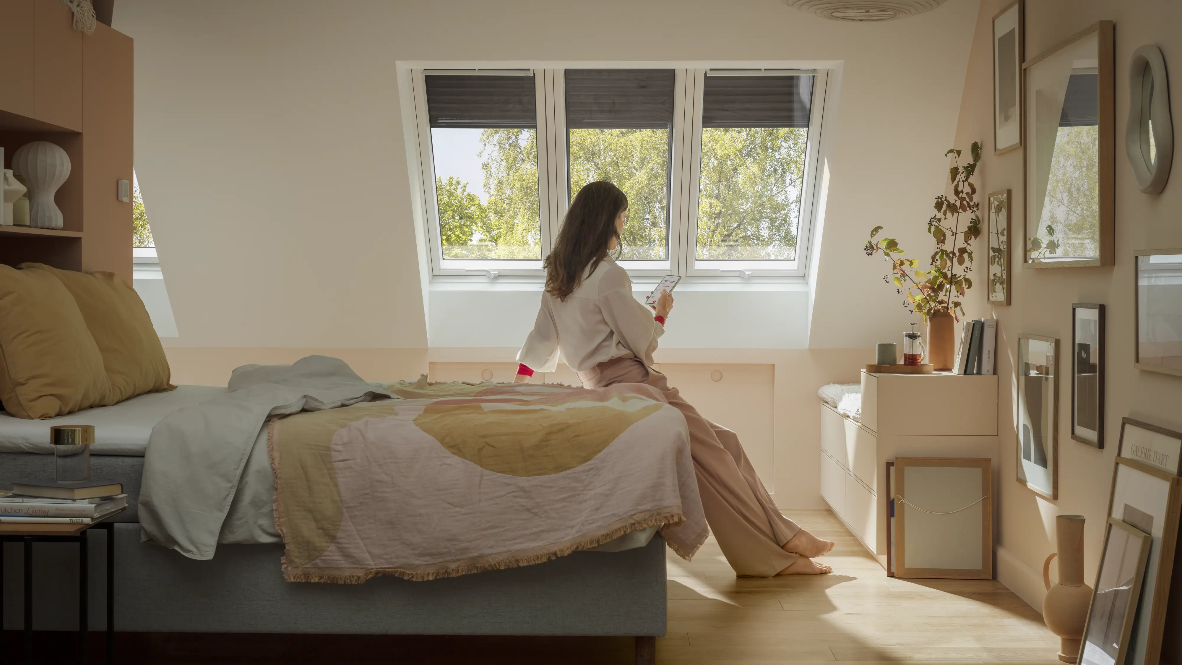 Attic bedroom with VELUX roof windows, woman sitting on bed, natural light.