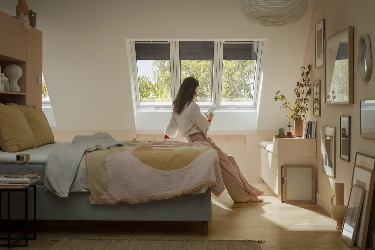 Žena sjedi na krevetu i gleda kroz svoje VELUX prozore.