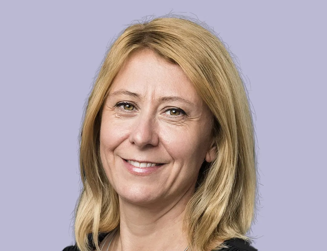 Woman with blonde hair, black outfit, and white bead necklace.