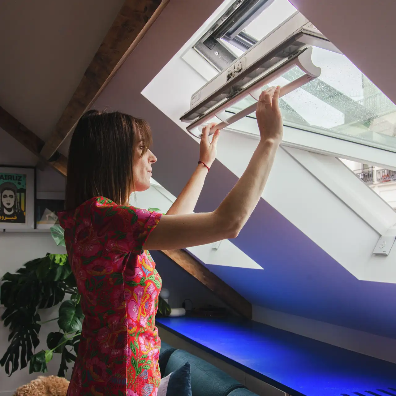 femme ouvrant une fenêtre de toit VELUX dans une pièce sous combles