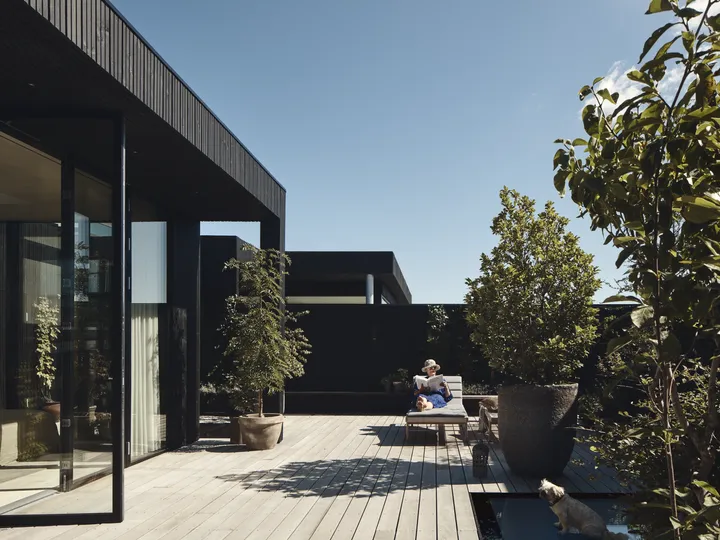 Frau mit Sonnenhut und -brille sonnt sich lesend auf der Liege ihrer Hausterrasse aus Holz | VELUX Magazin