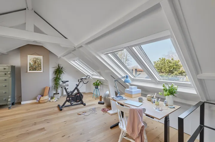 Таванско помещение със скосен таван, прозорци VELUX, бюро и велоергометър.