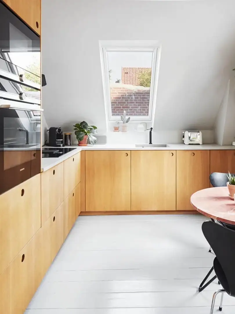 Cucina in legno chiaro con una finestra per tetti sopra il lavabo. 