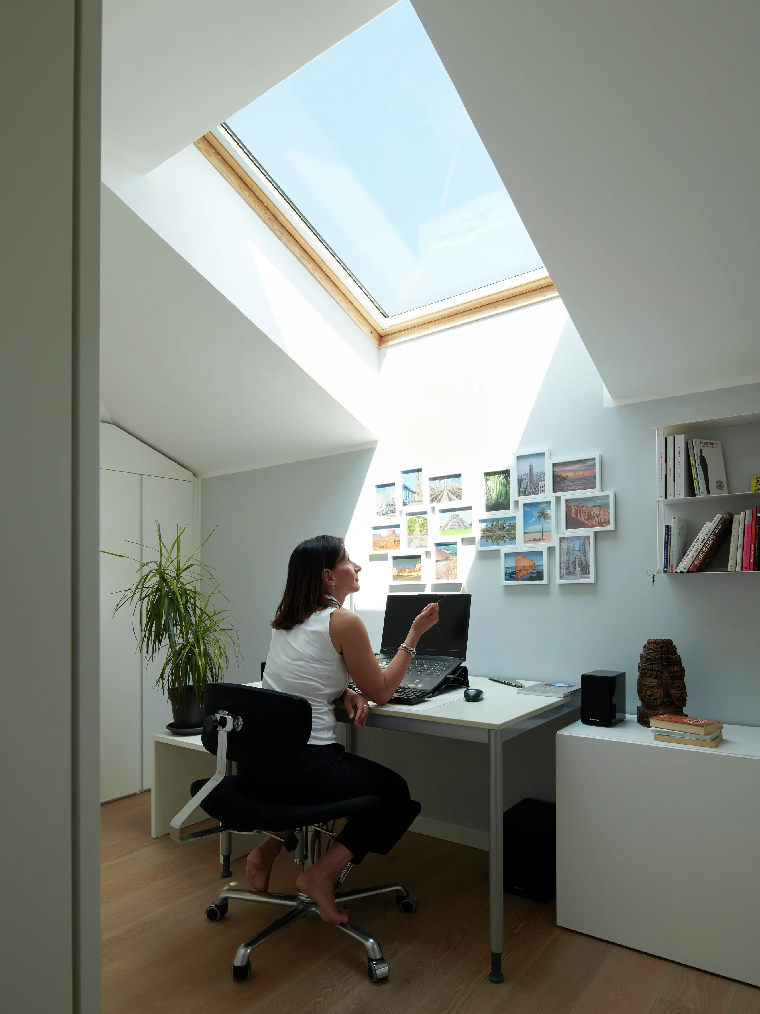 Angolo ufficio in casa con luce naturale proveniente da una finestra per tetti VELUX, piante e una scrivania in legno.