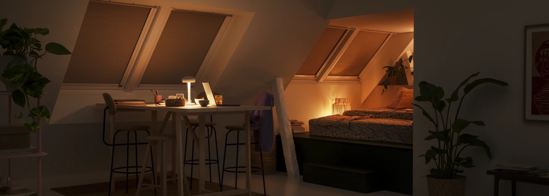 Attic room with sloped ceiling, VELUX roof windows with blinds, dining and bed area.