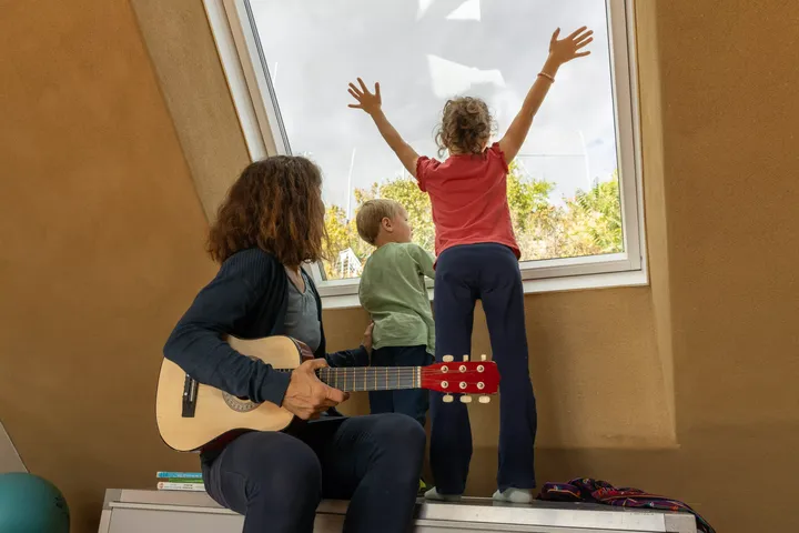 Mutter mit Gitarre sitzt unter dem Dachfenster und schaut mit ihren Kleinkindern ins Tageslicht | VELUX Magazin