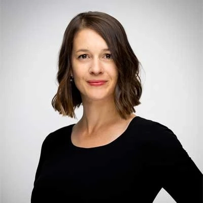 Woman in black top smiling confidently against a light grey background